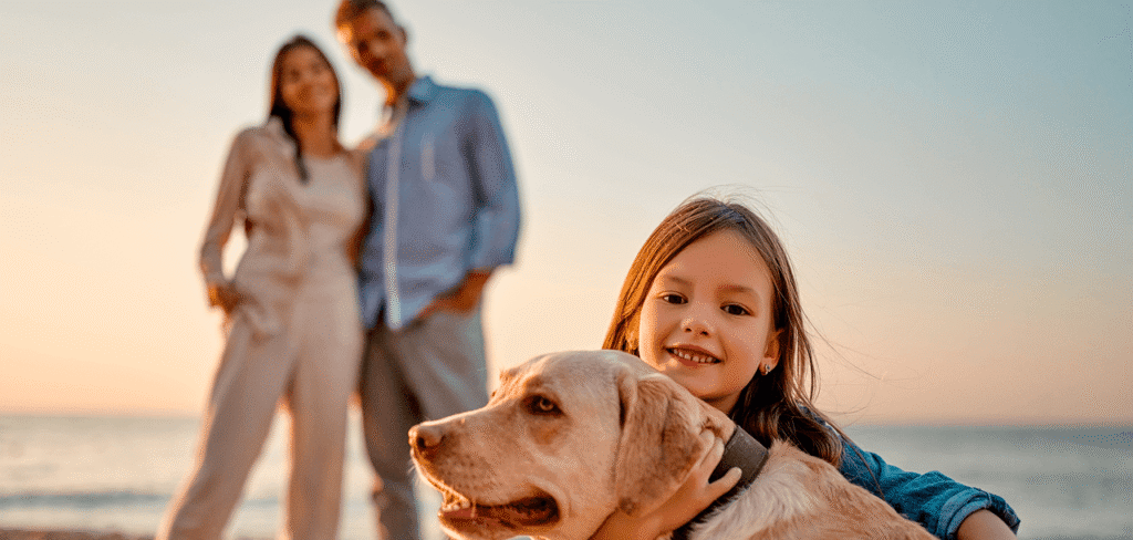 Family with young girl and dog on the beach at sunset